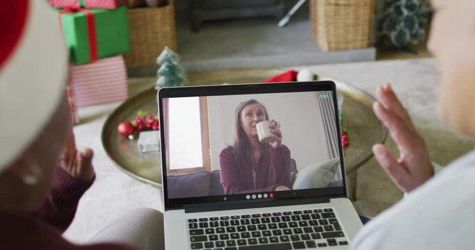 Diverse senior female friends using laptop for christmas video call with woman on screen