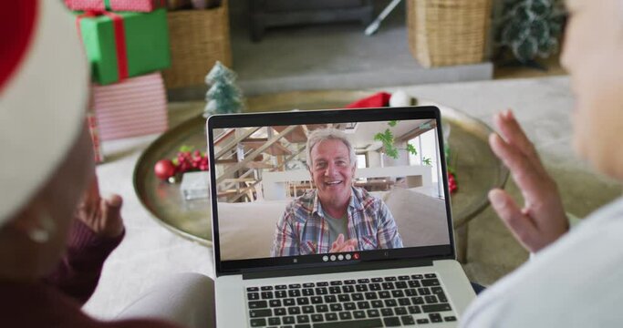 Diverse senior female friends using laptop for christmas video call with happy man on screen
