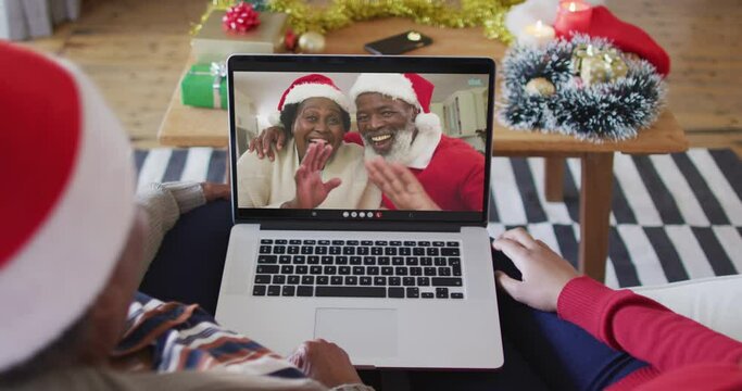 African american mother and daughter using laptop for christmas video call with couple on screen