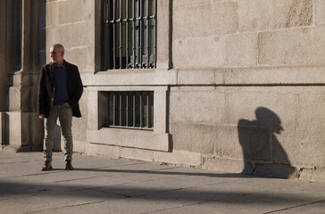 Adult man in suit standing on street against wall with sunlight and shadow