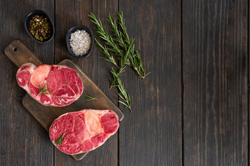 Two raw steaks of osso buco meat on wooden cut board with condiments and knife. Ingredients for  cooking