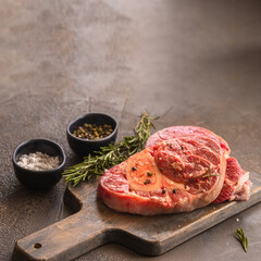 Two Osso bucco beef fillets on wooden cut board  with herbs on concrete table.Ossobuco alla Milanese recipe