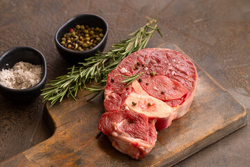 Two Osso bucco beef fillets on wooden cut board  with herbs on concrete table.Ossobuco alla Milanese recipe