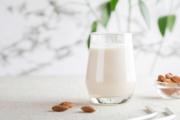 Vegan almond milk in glass with nuts on white background. Copy space. Healthy vegetarian food. selective focus. Non dairy alternative milk - obrazy, fototapety, plakaty
