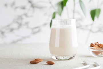 Fotobehang Vegan almond milk in glass with nuts on white background. Copy space. Healthy vegetarian food. selective focus. Non dairy alternative milk © Анна Мартьянова