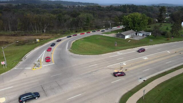 Corvette car parade through rural roads in Wisconsin. Cars turning onto highway. Residential home and garage on corner. Multiple directional signs present. 