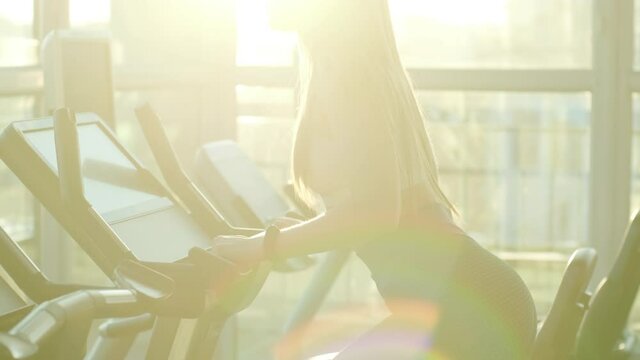Athlete woman is walking on orbitrek in gym. Girl is working out on stepper for cardio intensity and endurance improvement