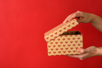 Hands holding opening Valentines gift box with hearts on red background