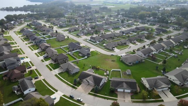 Aerial view of newer residential neighborhood in western Wisconsin. Symmetrical lines of larger homes and yards. Perfectly landscaped properties. Sunny sky and lake in corner.