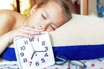 Girl sleeping on a pillow with an alarm clock in hand resting in the morning