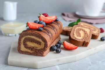 Tasty chocolate cake roll with cream and berries on light grey marble table
