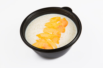 isolated close up top corner view shot of a delicious white rice milk porridge with peach fruit slices on top in a black plastic bowl on a white background