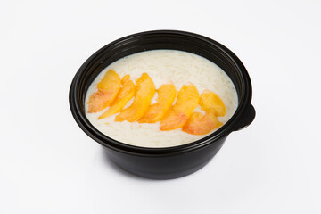 isolated close up top corner view shot of a delicious white rice milk porridge with peach fruit slices on top in a black plastic bowl on a white background