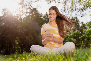 Full length body size photo woman sitting on grass smiling happy using smartphone browsing internet