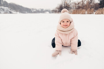 Happy laughing girl wearing a pink jacket, scarf and hat, playing in a beautiful snowy winter walk. Girl enjoys winter, frosty day. Playing with snow on winter holidays. Winter holidays concept.