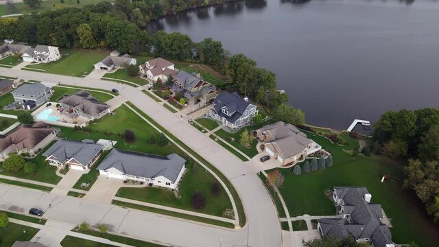 Aerial view of newer residential neighborhood in western Wisconsin. Symmetrical lines of larger homes and yards. Perfectly landscaped properties. Sunny sky and lake in corner.