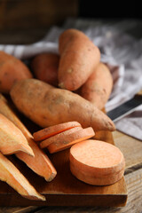Wooden board with cut and whole sweet potatoes on table, closeup