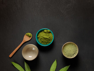 Green tea, matcha in Japanese bowls and powder from ground tea leaves. Top view on a black background. Horizontal, with space