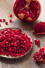 red pomegranate grains and fruit halves on a wooden table vertical frame