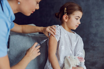 Obraz na płótnie Canvas Scared little girl sitting on sofa and getting vaccine.