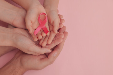 Family holding pink ribbon on color background, top view with space for text. Breast cancer...
