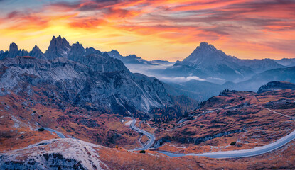 Dramatic  view of Tre Cime Di Lavaredo National Park with winding road. Misty morning scene of Dolomite Alps, Auronzo Di Cadore location. Sunrise in Italy. Beauty of nature concept background.