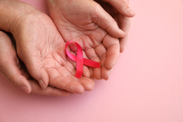 Senior woman and her adult daughter holding pink ribbon on color background, top view. Breast cancer awareness