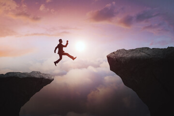 Businessman jumping from cliff on beautiful sky background. Gap, leap, risk, challenge and success concept.