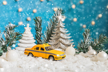 Christmas banner Background. Yellow toy car Taxi Cab model and winter decorations ornaments on blue background with snow. City traffic delivery taxi service concept
