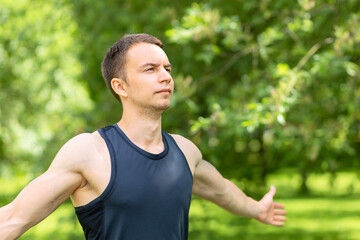 Relaxed young man breathing fresh air in forest with green trees. guy, athlete doing workout in nature in park.