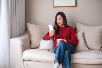 Obraz premium Portrait image of a beautiful young asian woman using mobile phone and earphones to listening to music or online chatting at home