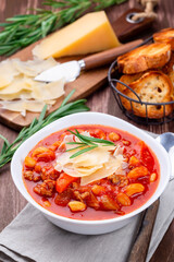 Minestrone soup served with crispy bread, on wooden background, vertical