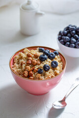 Herculean porridge with hazelnuts, granola and blueberries in a pink plate o white table. 