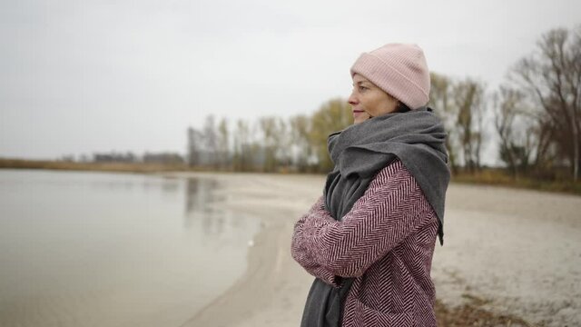 middle aged woman standing by the sea in winter and looking relaxed into the distance