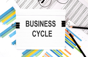 Notebook with pencils, glasses on graph background, with text BUSINESS CYCLE