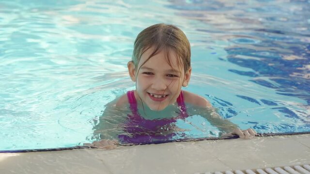 a funny little girl learns to swim without assistance at the side of the pool. 