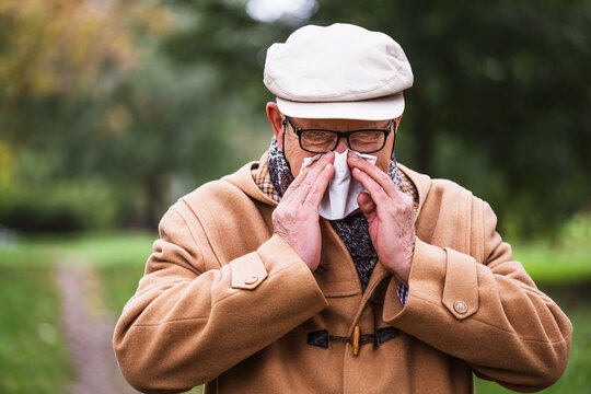 Outdoor portrait of senior man who is blowing nose in winter time in park.