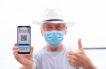 Senior man with hat shows  digital green pass, health passport app for people vaccinated against coronavirus, gesturing ok with hand