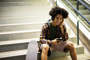 Cheerful guy listening music with the headphones. Young black man with curly hair enjoying in music