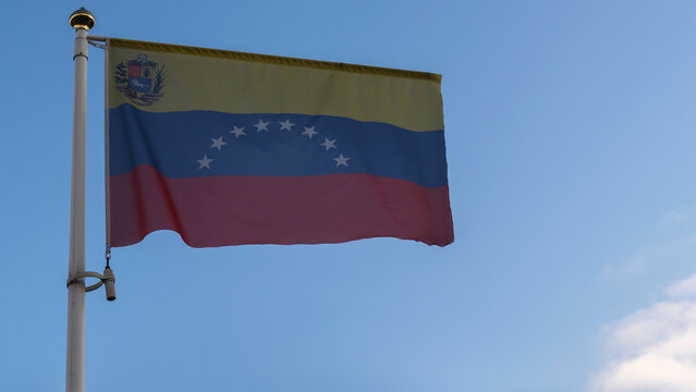 National flag of Venezuela on a flagpole in front of blue sky with sun rays and lens flare. Diplomacy concept.