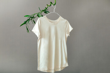 Beige T shirt hanging on hanger on plant Bamboo branches Isolated on gray background. Minimalistic...