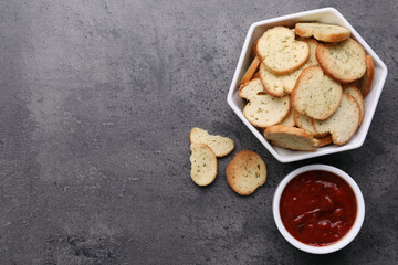 Crispy rusks and dip sauce on grey table, flat lay. Space for text