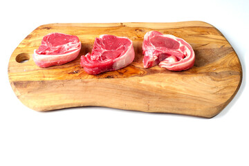 Three fresh lamb loin chops on a wooden board. Meat industry product, butcher craft and skill example.