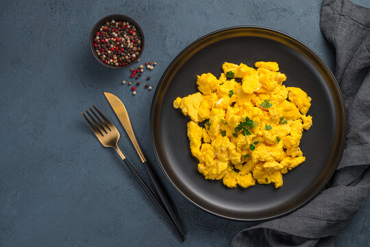 A portion of scrambled eggs with parsley on a dark background. Top view, horizontal. A recipe for home cooking.