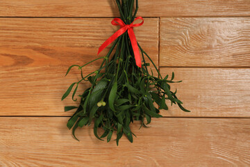 Mistletoe bunch with red bow on wooden table, top view. Traditional Christmas decor