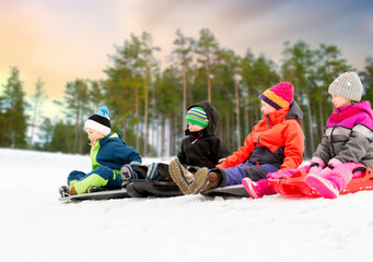 childhood, sledging and season concept - group of happy little children sliding on sleds in winter...