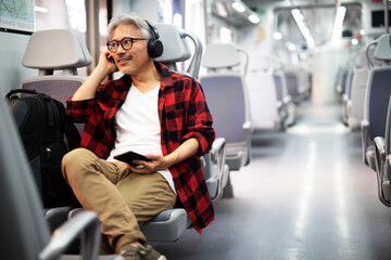 Fototapeta na wymiar Senior man traveling by train. Man listening the music while enjoying in travel.