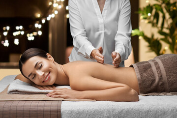 wellness, beauty and relaxation concept - beautiful young woman lying and having back massage at spa over christmas lights on window background