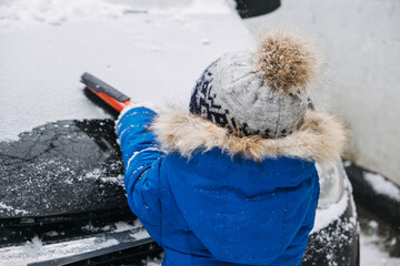 Cute little boy cleaning snow off the car at winter backyard. Little kid Toddler boy helping father...