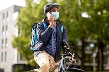 food shipping, health and people concept - indian delivery man in bike helmet and mask with thermal insulated bag and smatphone riding bicycle on city street